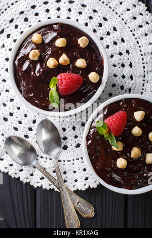 Delicious chocolate pudding with hazelnuts and raspberries close-up in a bowl on the table. Vertical top view from above Stock Photo