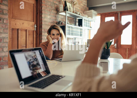 Young woman sitting at table with laptop and looking at boyfriend in front at home. Stock Photo