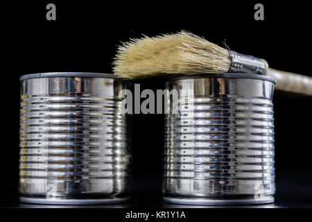 Cans of paint on a wooden workshop table. Next to the pedals and paint rollers. Black background Stock Photo