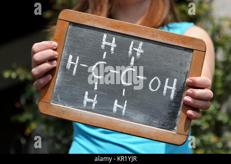 chemical formula for ethanol written with chalk on slate shown by young female Stock Photo