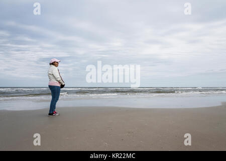 Woman wearing a Coat, Hat and Gloves and by herself on New Smyrna Beach Shoreline, Florida USA Stock Photo