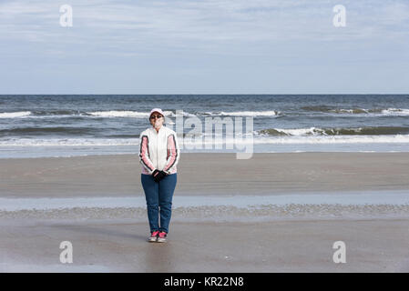 Woman wearing a Coat, Hat and Gloves and by herself on New Smyrna Beach Shoreline, Florida USA Stock Photo