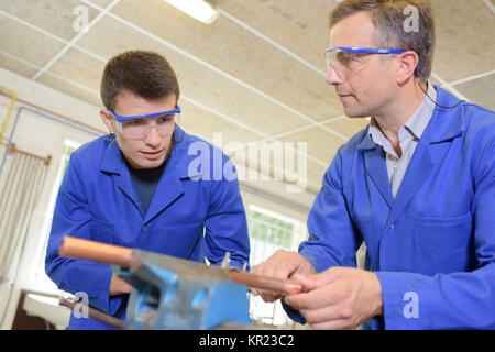 Two men working on copper pipe held in vice Stock Photo