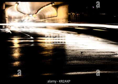 Blurry night traffic in tunnel and on rainy city streets intersection with light trails and reflections on wet asphalt. Stock Photo