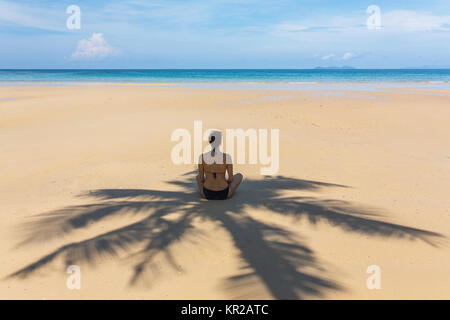 Young woman sitting in the shadow of palm tree on tropical beach on Koh Kood island, Thailand Stock Photo