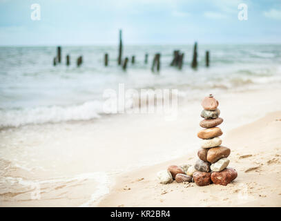 Pyramid of stones on the seashore on the background of black sticks in the sea Stock Photo