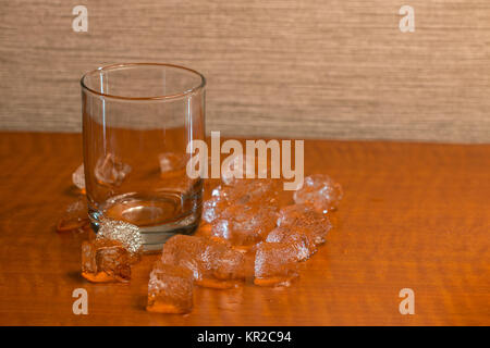 Empty Glass on Wooden Table with Ice Cubes Around it Stock Photo