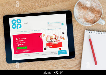 The Coop Food website on an iPad tablet device which rests on a wooden table beside a notepad and pencil and a cup of coffee (Editorial only) Stock Photo