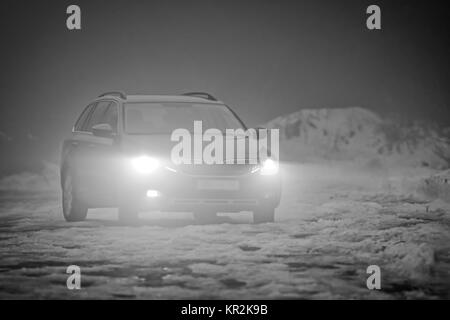 The greyscale photo of car with the lights on in the fog Stock Photo