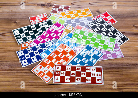 Colorful lotto or bingo game papers with numbers and plastic lotto barrels, on wooden background. Stock Photo