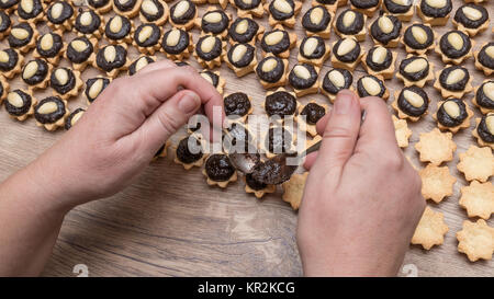 Preparation of sweet coconut cupcakes with cocoa filling and almonds. Female hands putting chocolate on the Christmas pastries stacked on wooden table. Stock Photo