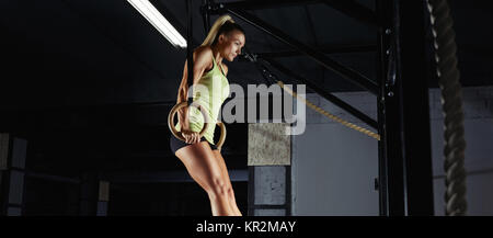 Low angle shot of a sportswoman doing ring dips at the crossfit gym. Gorgeous young woman performing crossfit workout complex using gymnastic rings at Stock Photo