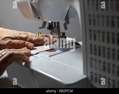 Hands holding fabric while operating a sewing machine - selective focus and motion Stock Photo