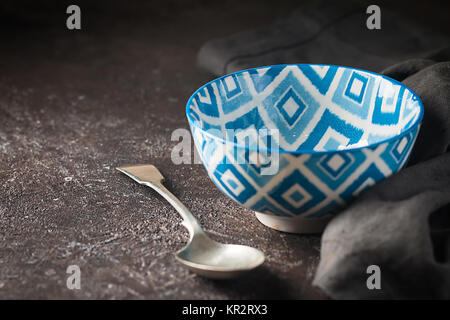 Empty blue oriental bowl with a spoon on dark stone background. Stock Photo