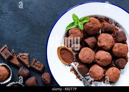 Homemade raw chocolate truffles decorated with mint on white plate and pieces of dark chocolate. Table top view, copy space for your text. Stock Photo