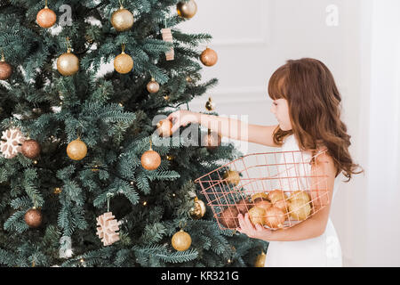 Beautiful little girl decorates huge Christmas tree for holiday celebration. Horizontal color photography. Stock Photo