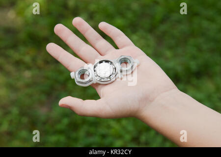 Closeup of hand of white kid playing modern popular hand toy spinner made by himself by using screw-nuts and bearing. Child holding unusual metal spin Stock Photo