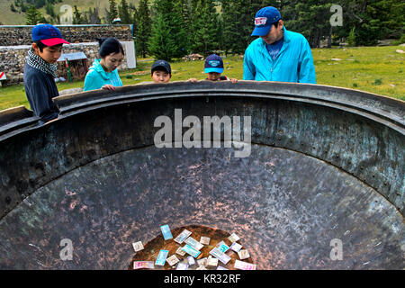 Visitors looking at banknotes lying in the giant bronze cauldron of the Manzushir Monastery, Zuunmod, Töv Province, Mongolia Stock Photo