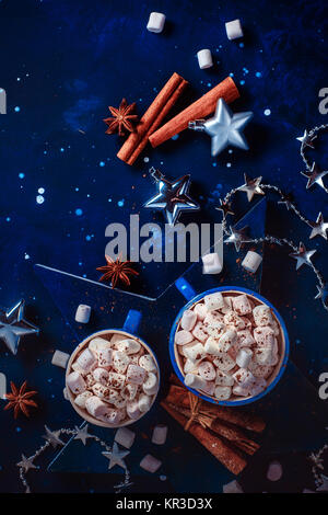 Christmas flat lay with silver toys, decorations, cinnamon, anise stars and hot chocolate with marshmallows on a deep blue wooden background. New Year Stock Photo