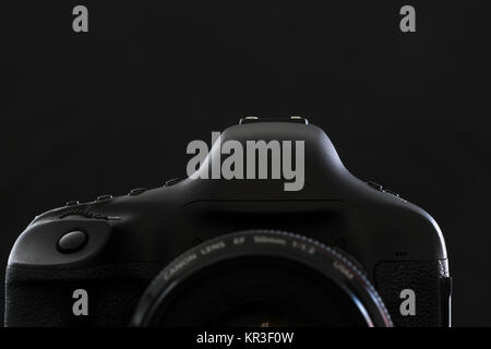 Professional modern DSLR camera low key stock photo/image - Modern DSLR camera with a very wide aperture lens on with highlighted edges against black background Stock Photo