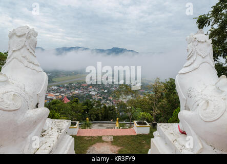 Lion statue at Wat Phra That Doi Kong Mu with city view of Mae Hong Son in the mist, Thailand Stock Photo