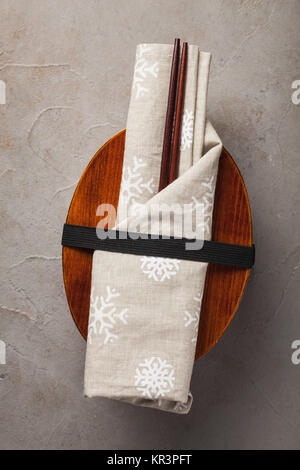 Closed wooden Japanese lunchbox with chopsticks, wrapped in a festive cloth on an old stone table. Top view. Stock Photo