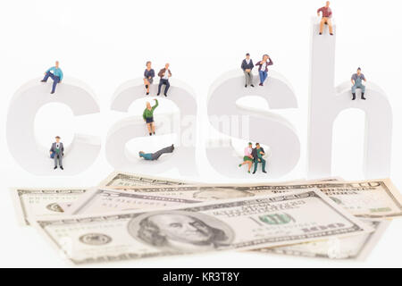 Miniature people sitting on cash wooden letters Stock Photo