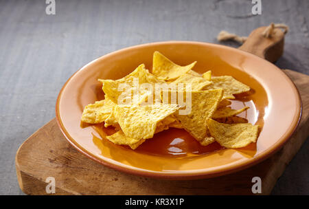 Single plate of tasty yellow tortilla chips on thick wooden cutting board over gray table with copy space Stock Photo