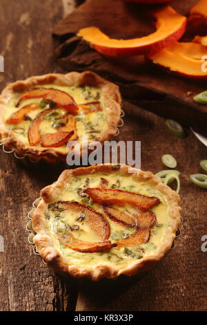 Tasty homemade butternut quiche or flans with a crispy pastry crust and slices of squash in a custard and herb base on a rustic wooden table Stock Photo