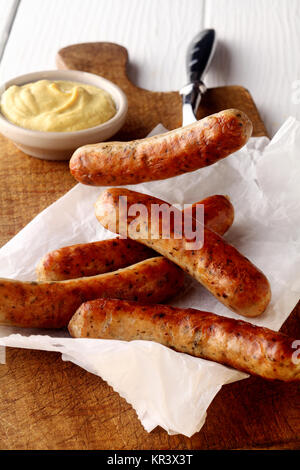 Five spicy grilled sausages with mustard dip on crumpled white oven paper on a cutting board conceptual of summer picnics and barbecues Stock Photo