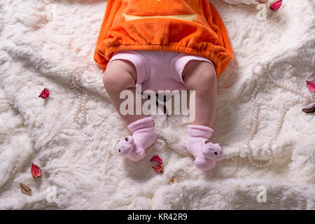 Body parts of a baby girl with orange sweater and pink pant on white soft blanket, top view. Stock Photo