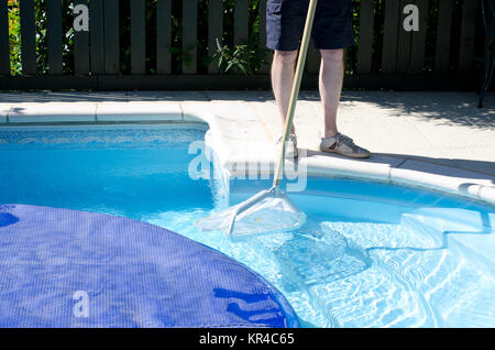 A man with a net cleaning the last part of the swimming pool before the cover goes on Stock Photo