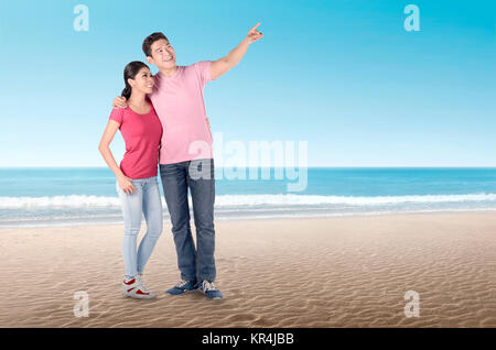 Happy asian couple embracing and pointing to sky on the beach Stock Photo