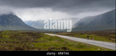 Glencoe, Scotland, UK - June 4, 2011: A cyclist on the A82 road is dwarfed by the vast expanse of Rannoch Moor and the mountains of Glen Coe in the We Stock Photo