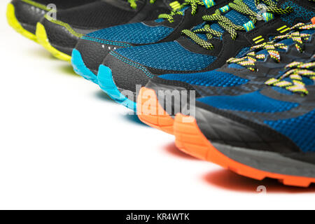 Three pairs of colourful exercise trainers / running shoes lined up in a row on a white floor with copy space. Stock Photo