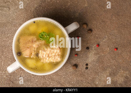 top view of fresh transparent fish soup with sturgeon, potatoes in white plate, decorated black and pink dry peppers, healthy eating, copy space Stock Photo