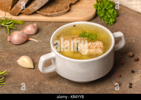 fresh transparent fish soup with sturgeon, potatoes in white plate, decorated garlic, parsley leaves and cutted rye bread, healthy eating Stock Photo