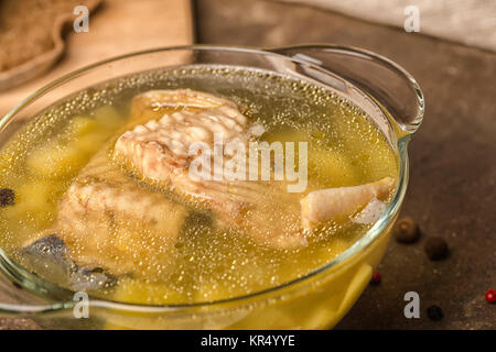 fresh fish soup with sturgeon, potatoes in transparent plate, decorated spices and rye bread on stone background, healthy eating, close up Stock Photo