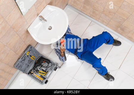 Plumber Lying On Floor Repairing Sink In Bathroom Stock Photo
