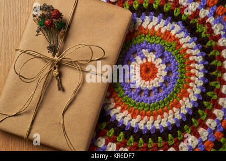 Wrapped book tied with brown paper thread with small dried bouquet of field plants is lying on the table on colorful knitted napkin. Stock Photo