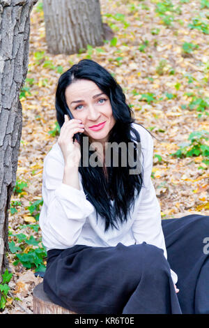 Brunette talking by cellular in autumn park Stock Photo