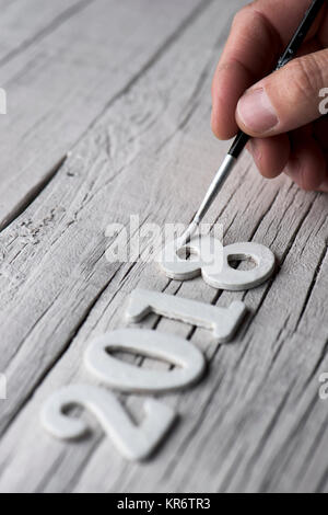 closeup of a young caucasian man painting white the four numbers of the number 2018, as the new year, on a rustic white wooden background Stock Photo