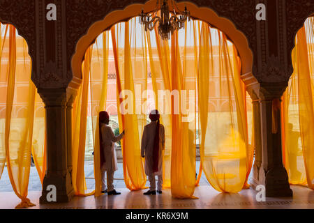 Two men wearing traditional clothing and turbans standing under arch decorated with translucent orange curtains. Stock Photo