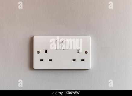 UK domestic 3 pin double plug electrical socket in white plastic on a beige coloured wall Stock Photo