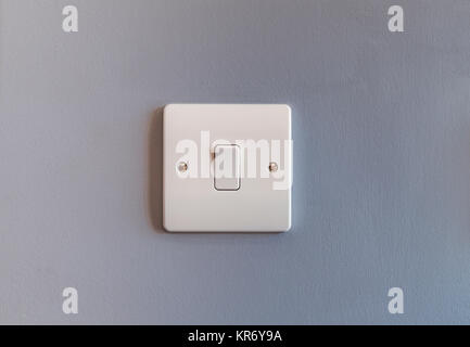 UK domestic single light switch in white plastic on a grey coloured wall Stock Photo