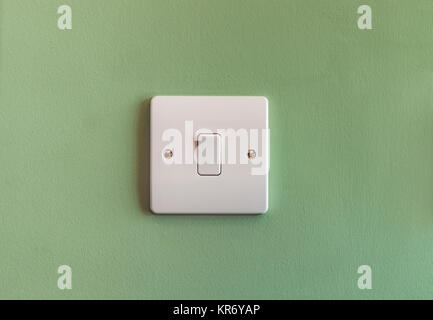 UK domestic single light switch in white plastic on a green coloured wall Stock Photo