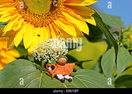 small gnome with flower umbrella sitting on sunflower leaf Stock Photo