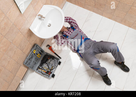 Male Plumber Lying On Floor Repairing Sink In Bathroom Stock Photo