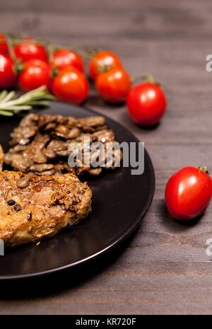 Pork steak in black plate with grilled mushrooms, oregano cherry Stock Photo