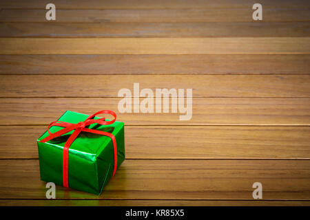 Metallic green gift package with red ribbon on a wooden background. Stock Photo